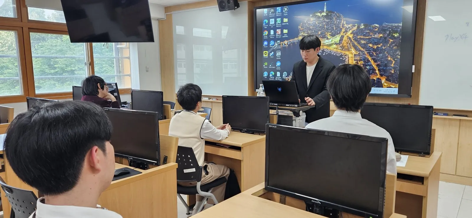 교실에서 대학생 멘토가 전자칠판에 코드를 띄우고 설명하는 장면